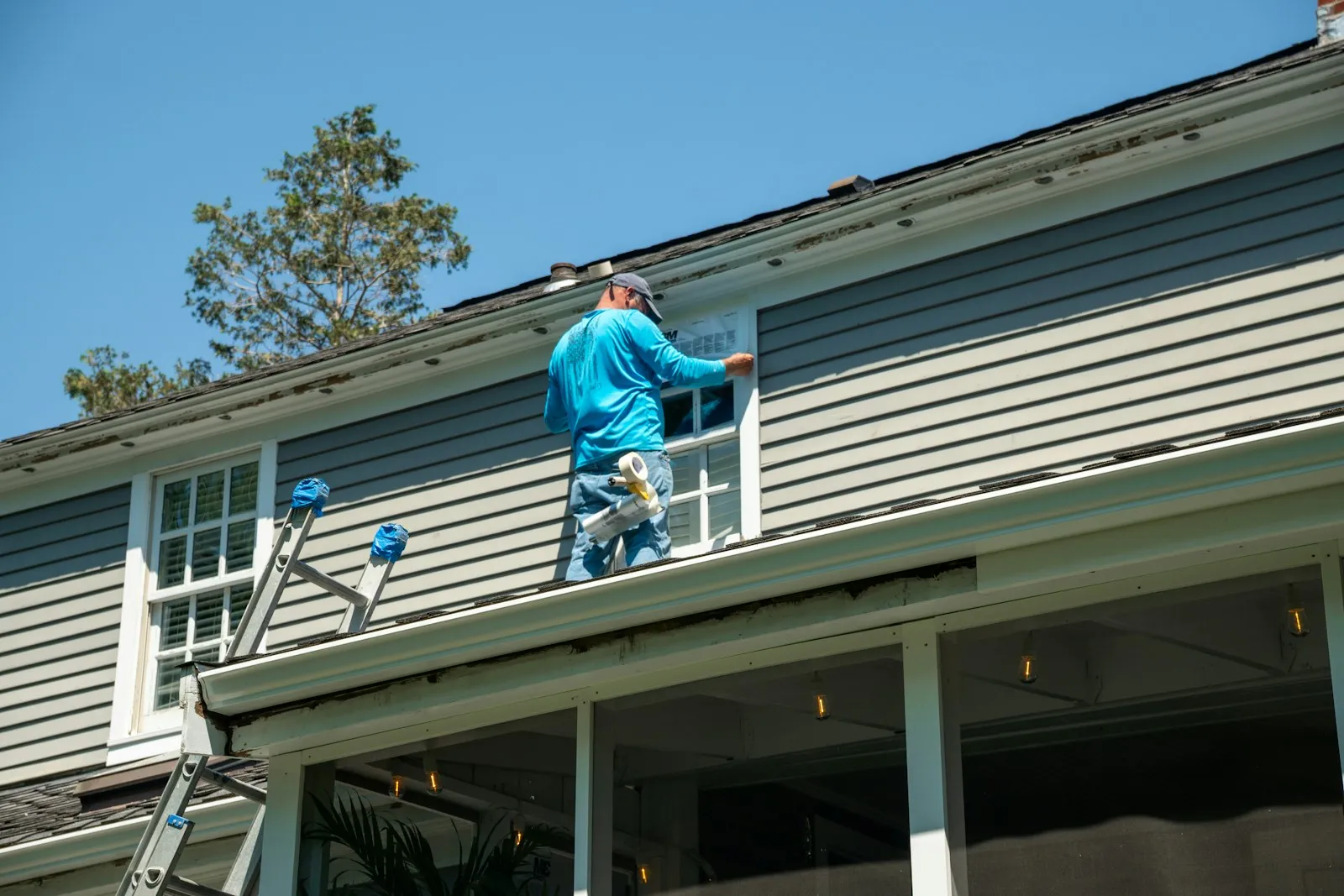 Construction worker on a ladder installing window flashing during a house renovation
