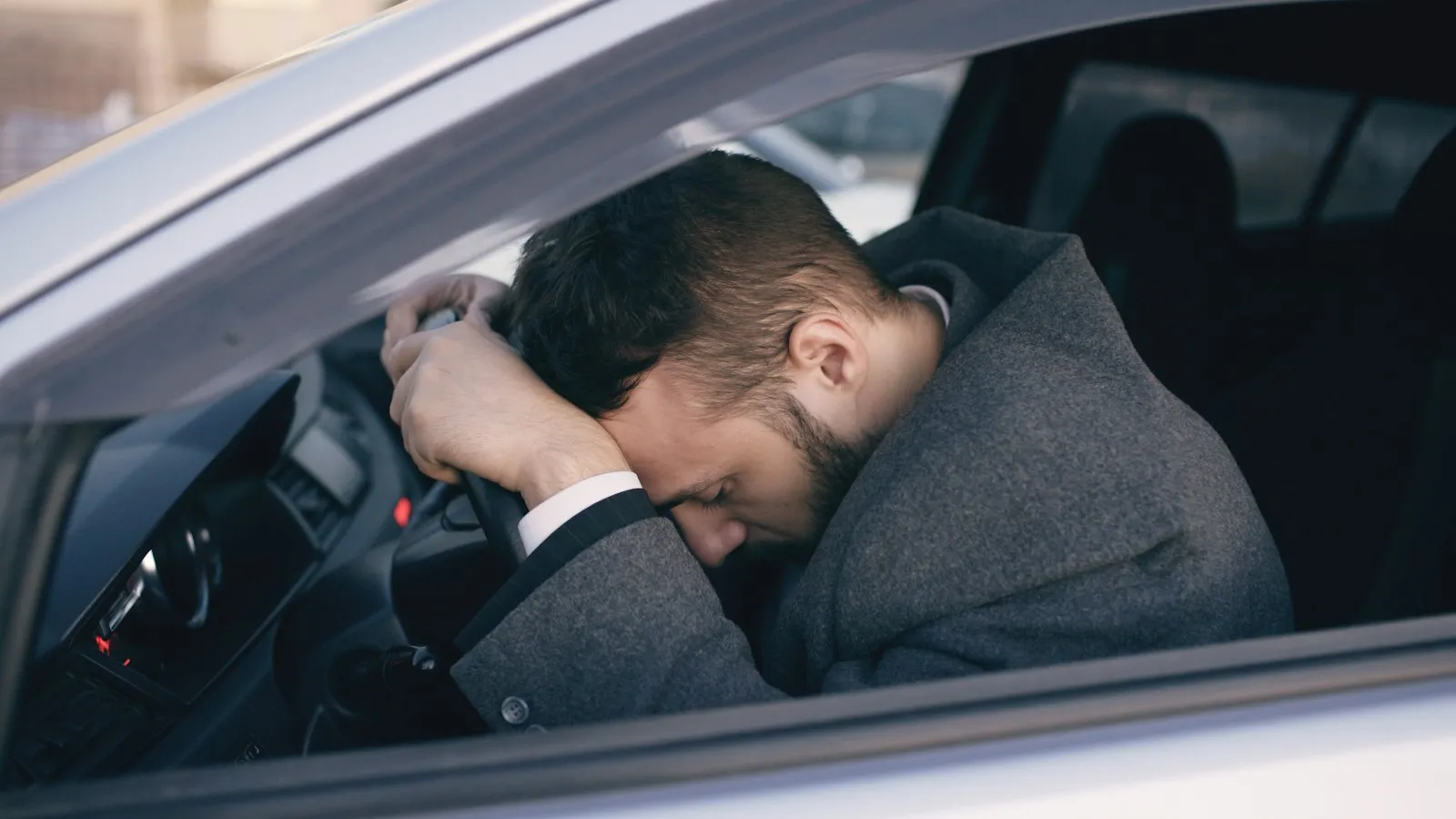Exhausted man resting his head on his hand at the steering wheel, the kind of fatigue a drowsy driving lawyer must prove