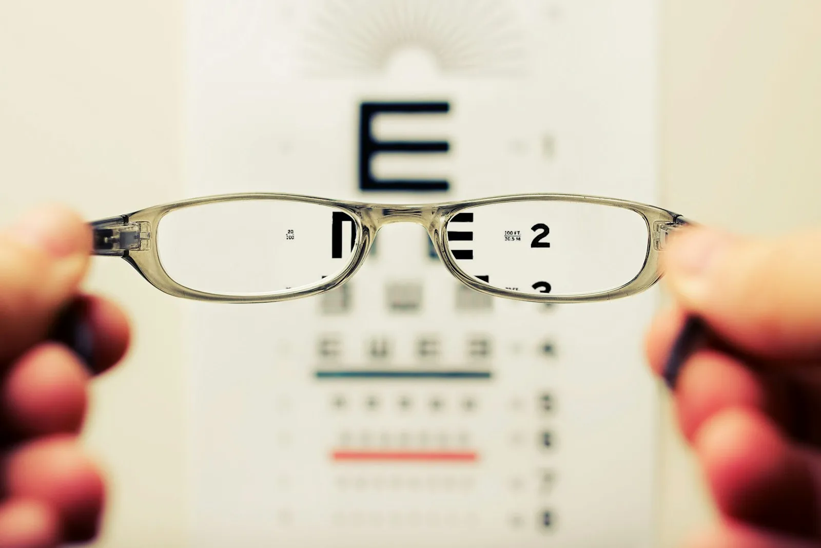 Hands holding eyeglasses up in front of an eye chart, eye injury lawyer vision loss damages