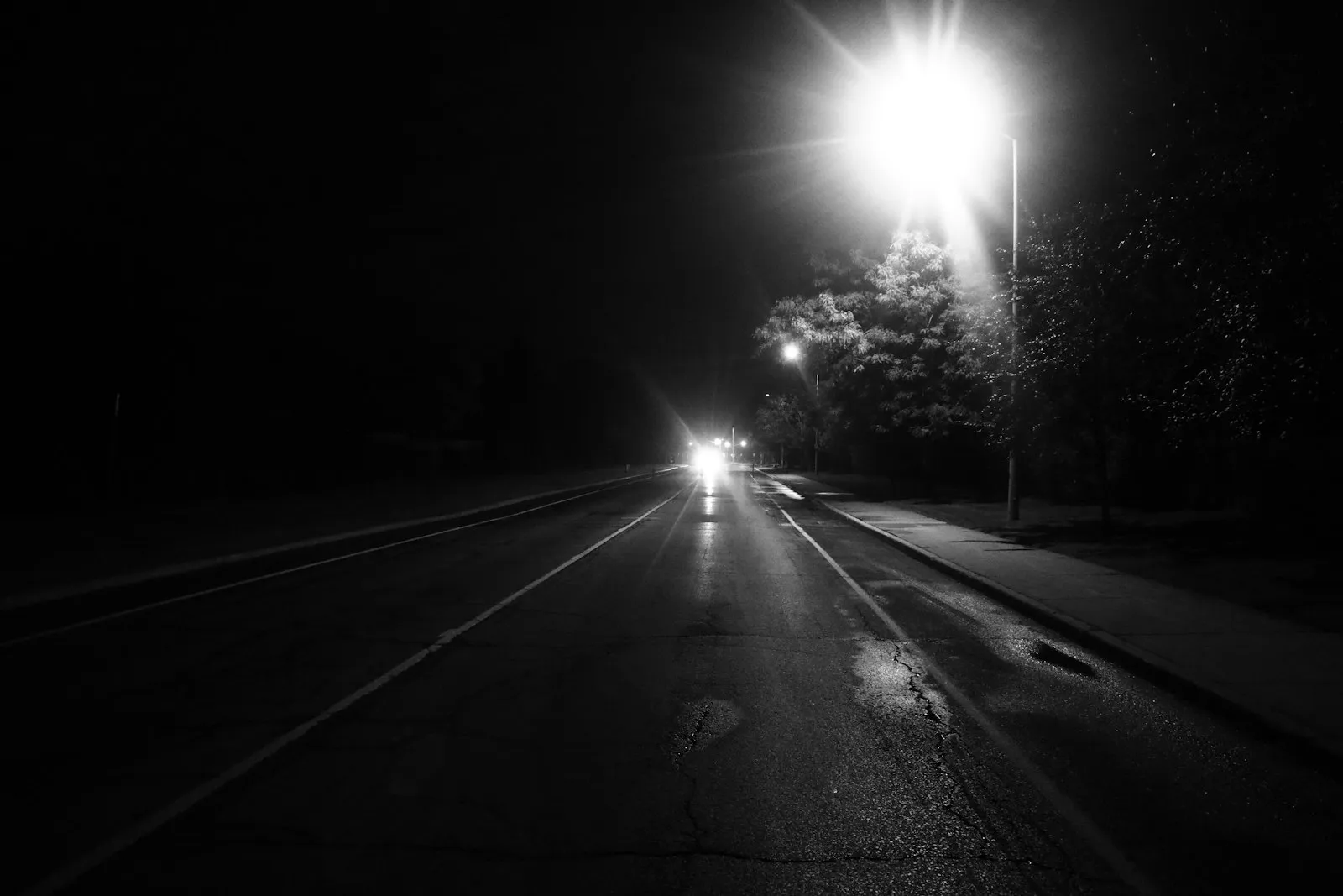 Dark two-lane road at night with oncoming headlights and a streetlight, illustrating the risks a head on collision lawyer investigates