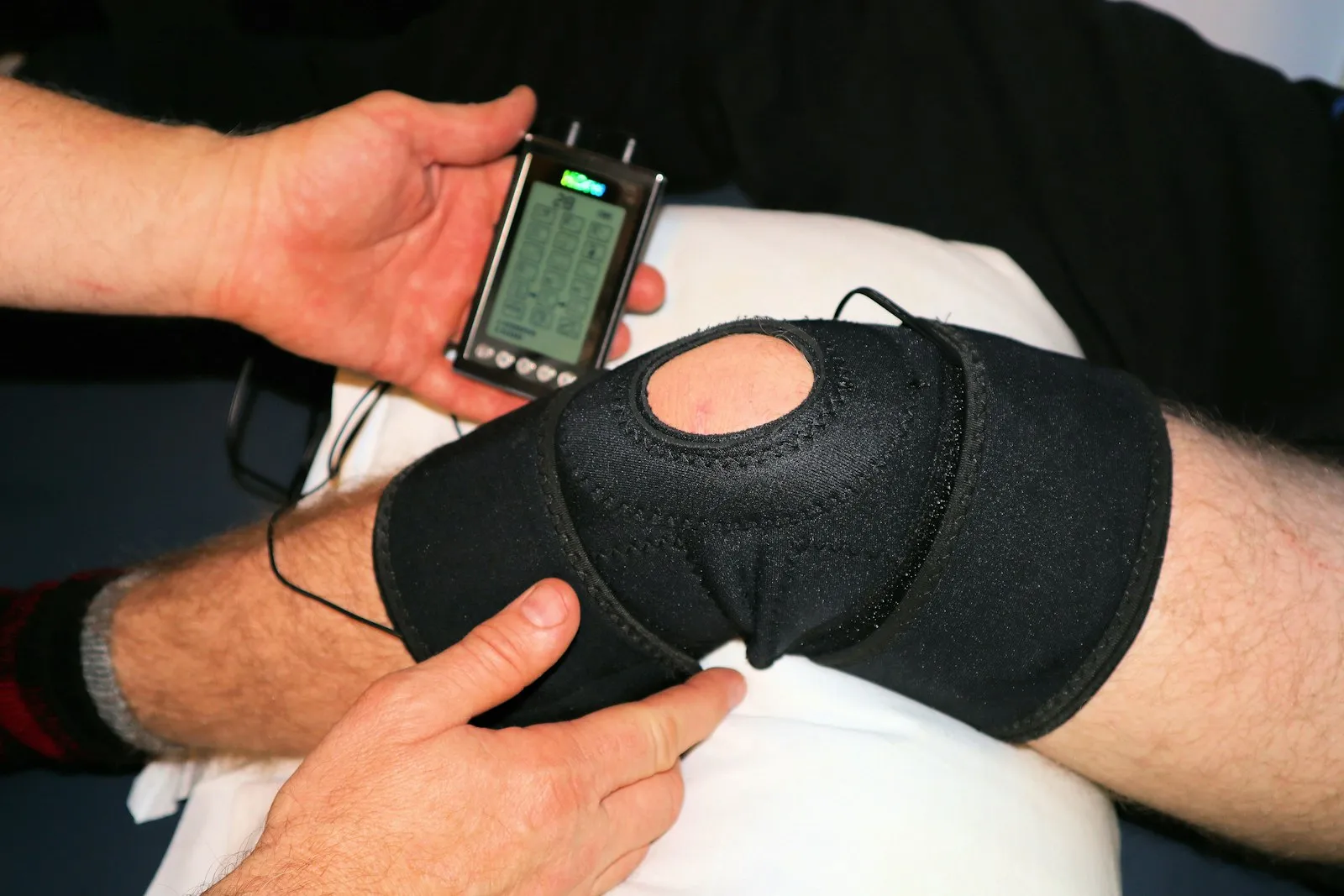 Une genouillère noire connectée à une unité de stimulation électrique portative, partie de la réadaptation du genou qu'un avocat documente