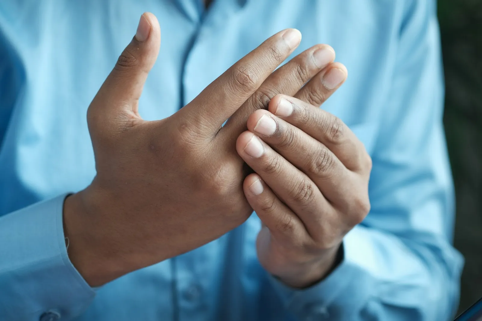 Man in a blue shirt holding his hand in pain from a nerve injury, a common concern for a nerve damage lawyer