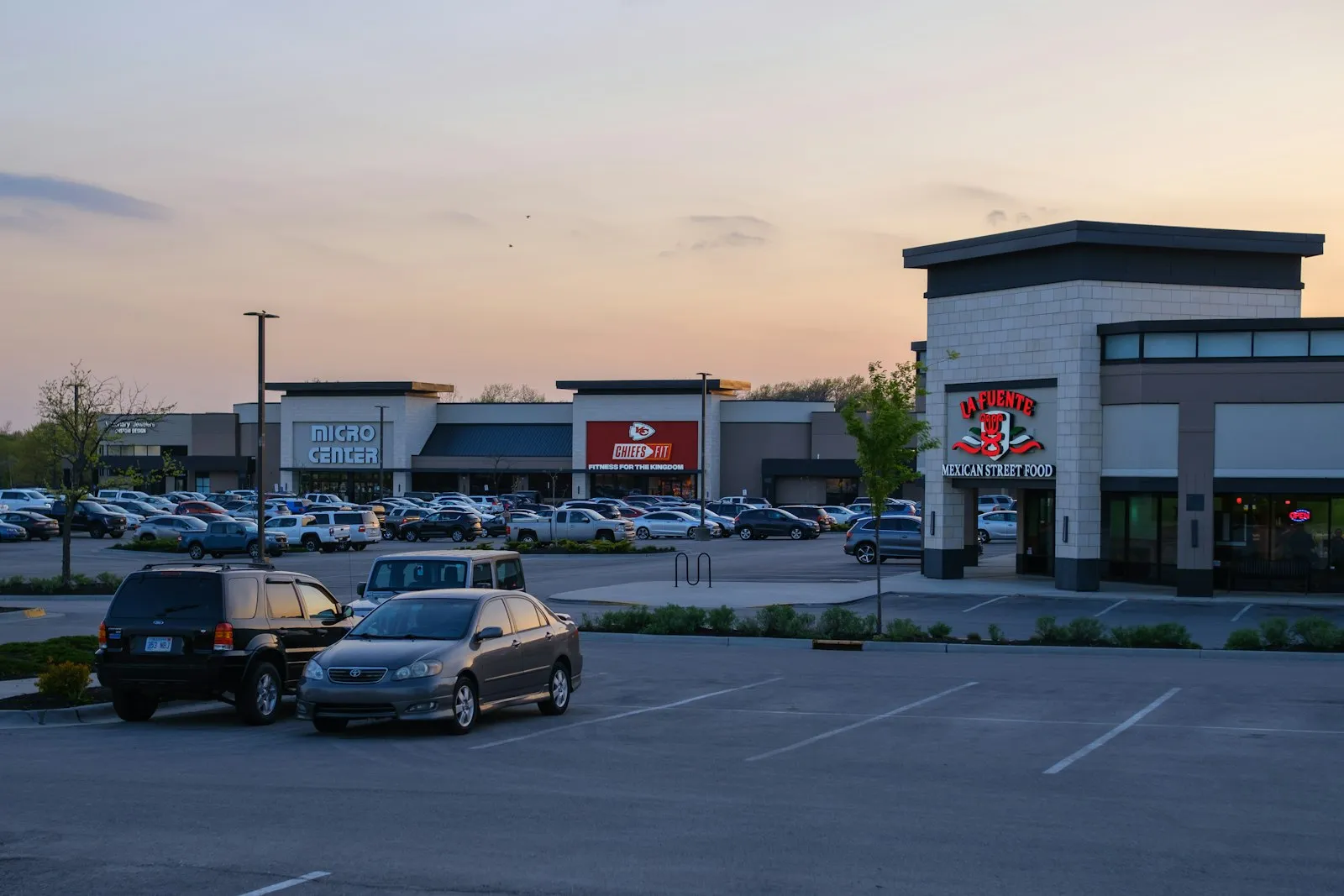 Shopping center parking lot with cars in front of retail stores at dusk, relevant to a parking lot accident attorney