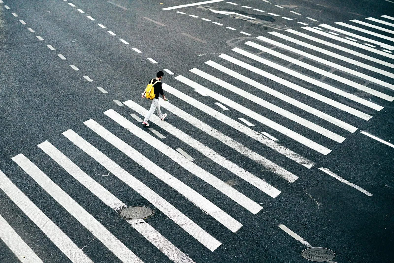 Overhead view of a lone pedestrian on a wide striped crosswalk, for a pedestrian accident lawyer guide