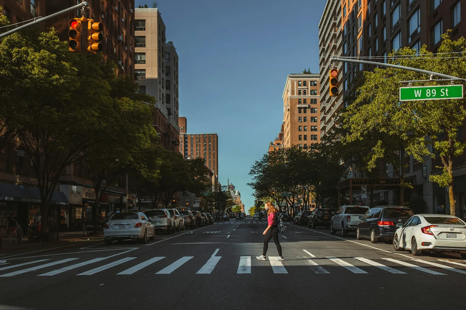 Pedestrian crossing a tree-lined city avenue in a marked crosswalk, illustrating a pedestrian accident lawyer's settlement guide