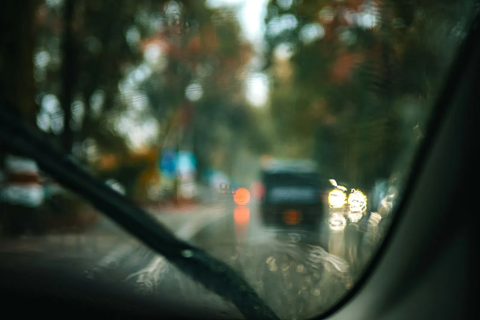 Rainy windshield view of blurred traffic lights