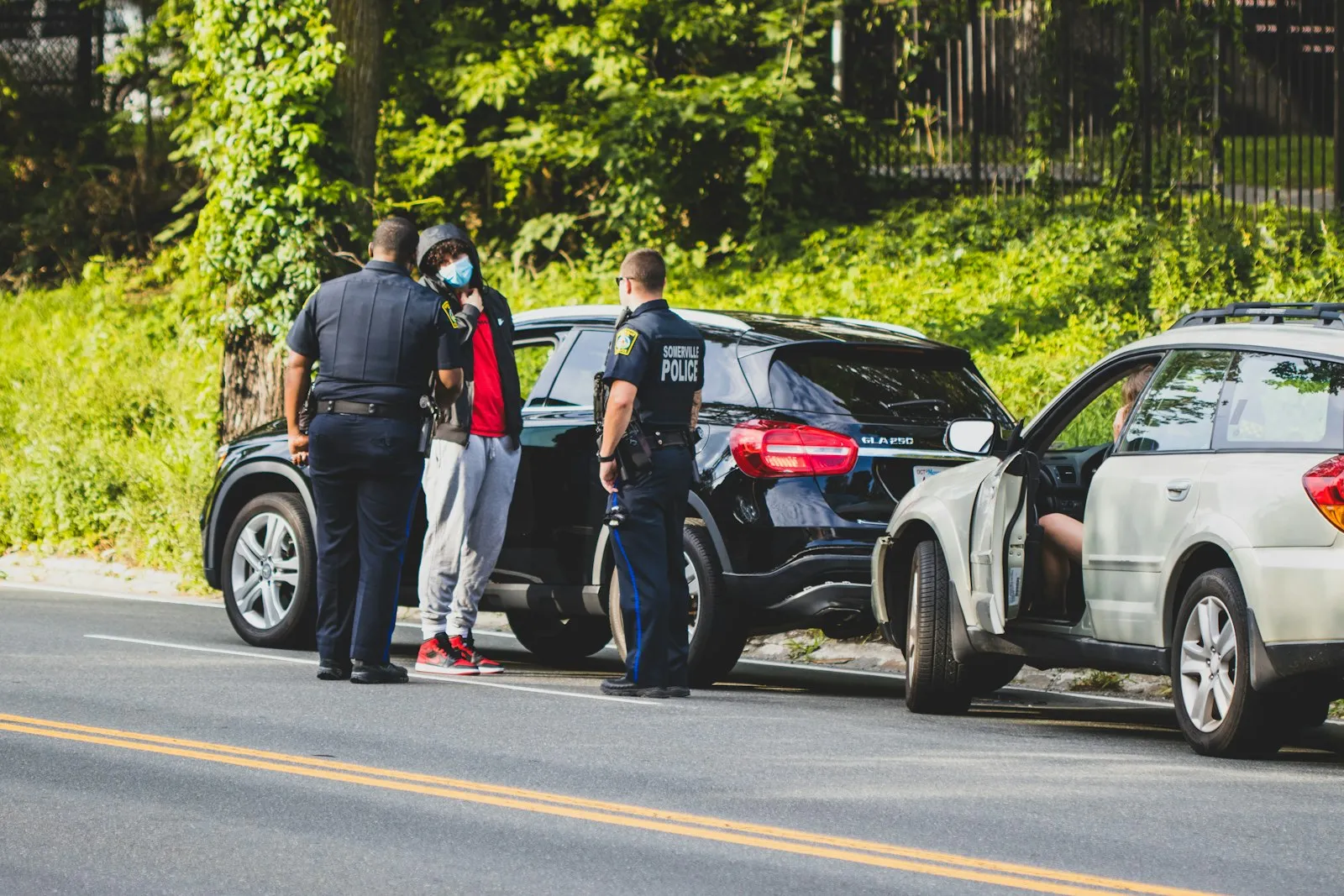 Police officers speaking with a driver beside two SUVs at the roadside after a rollover crash, lawyer review pending