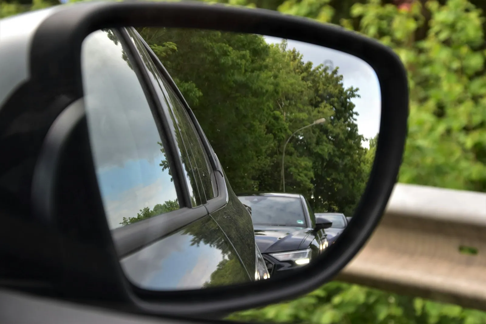 Car side mirror reflecting a vehicle travelling alongside, illustrating blind spots for a sideswipe accident lawyer post