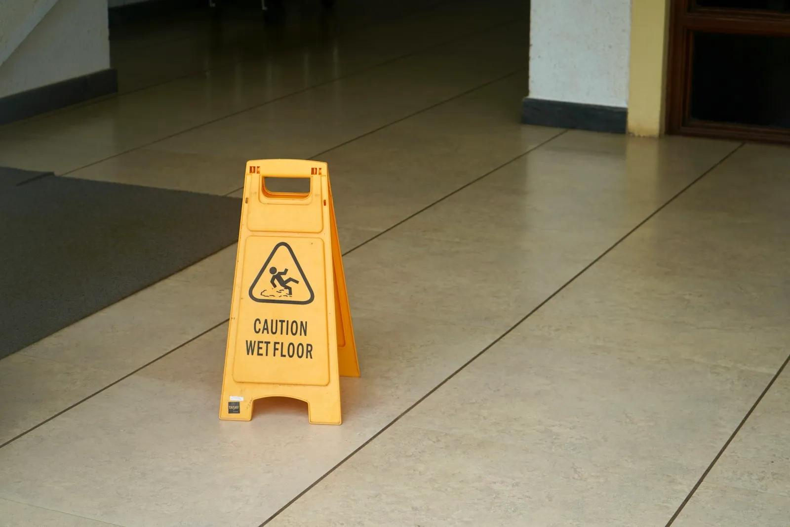 Cartello di avvertimento giallo in piedi su un pavimento piastrellato, un dettaglio che un avvocato specializzato in lesioni di Valley Stream documenta come prova