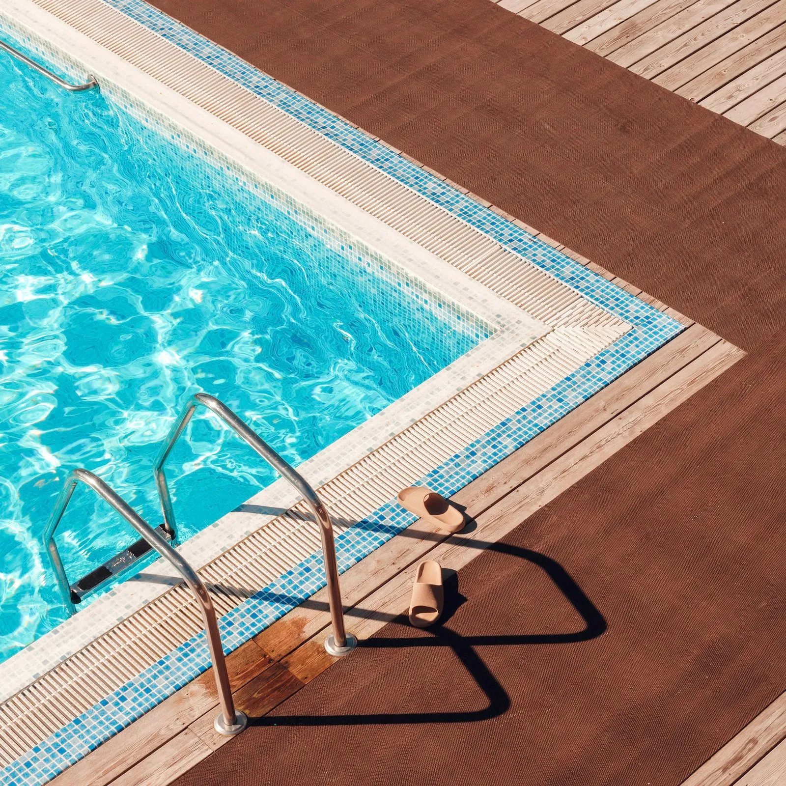 Metal pool ladder leading into a pool from a wooden deck, a common swimming pool injury point a lawyer examines